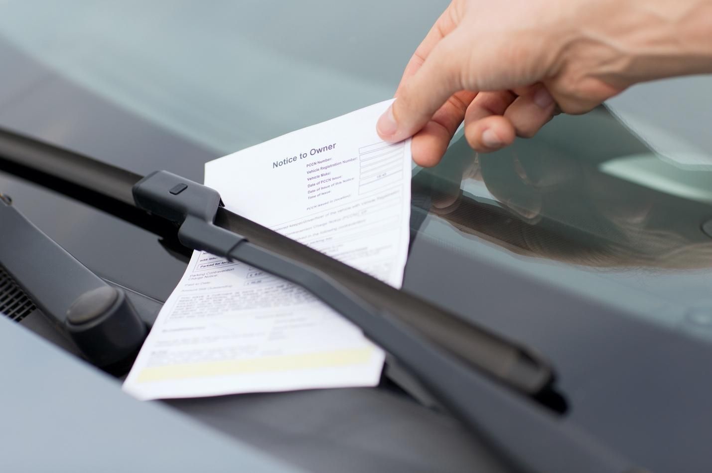 A driver lifting a parking ticket off their windshield.