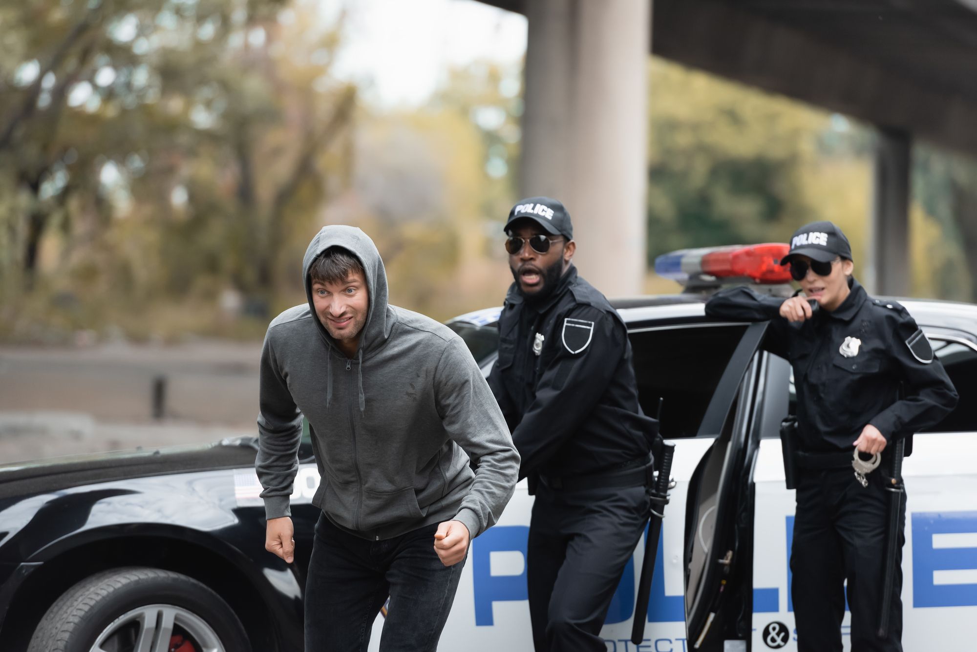 Caucasian male in hooded sweatshirt fleeing on foot, pursued by uniformed police officers; eluding the police.