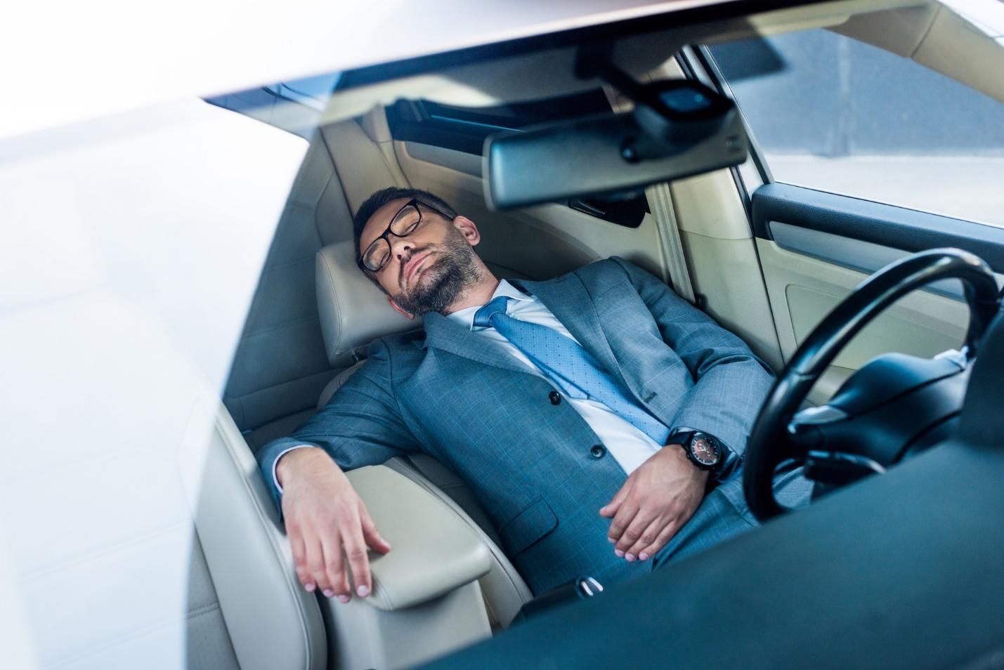 Man in suit asleep in reclined driver’s seat of car