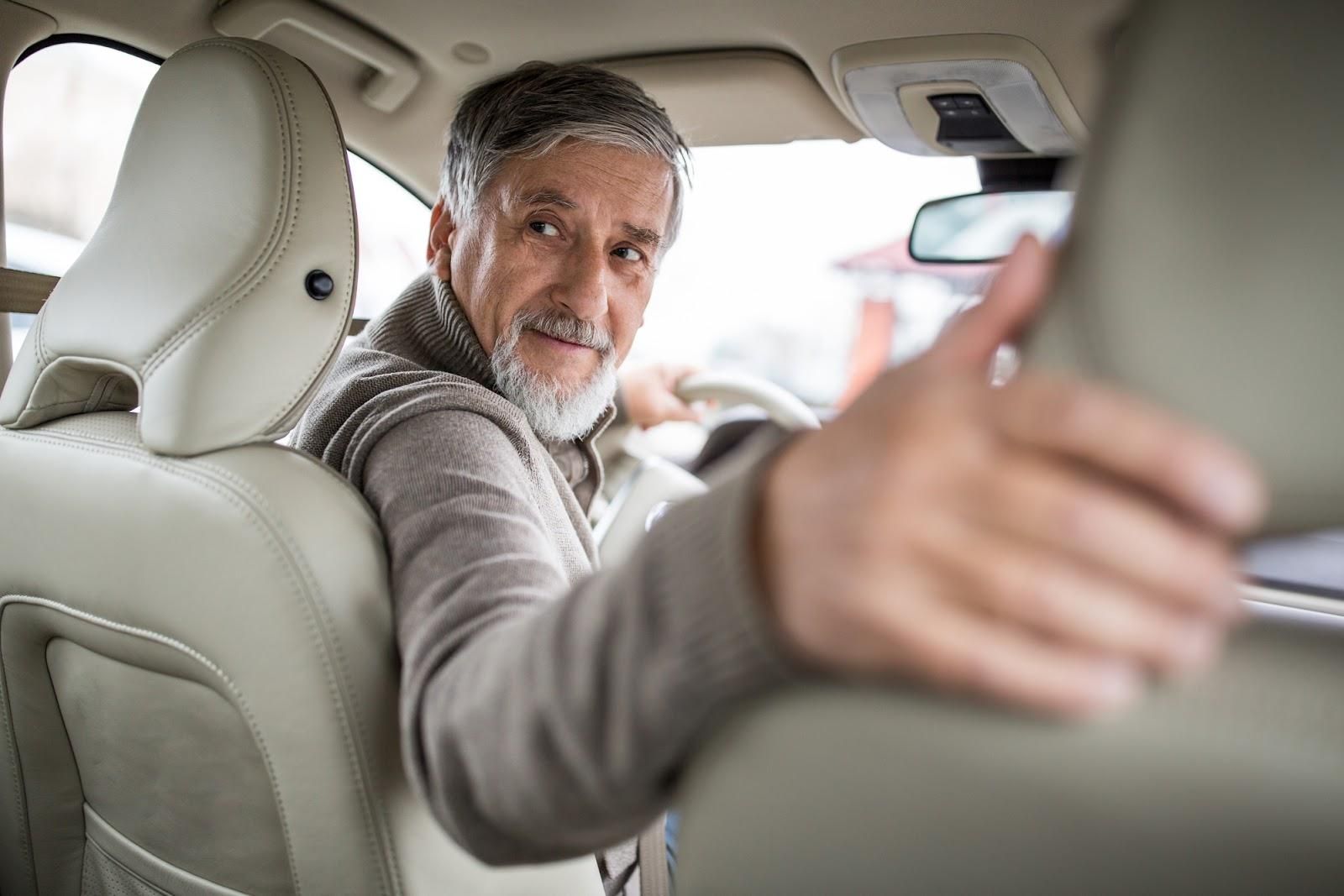 Gray-haired man in sweater turning to check blind spots before reversing his vehicle to avoid improper backing