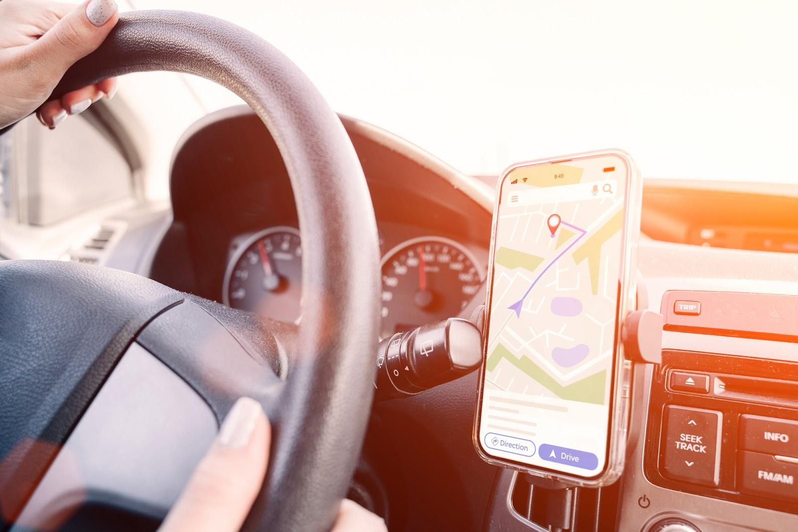 A phone using a safe driving app to help the navigator find their location rests in a hands-free phone holder to comply with state laws.