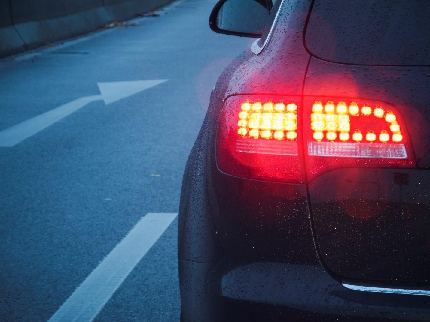 The left brake light of a black car at dusk.