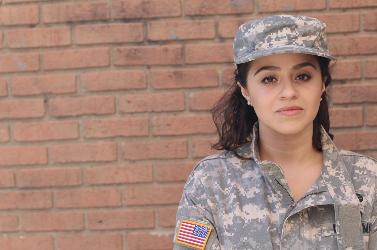 Photograph of a young woman in United States military fatigues, looking tired.