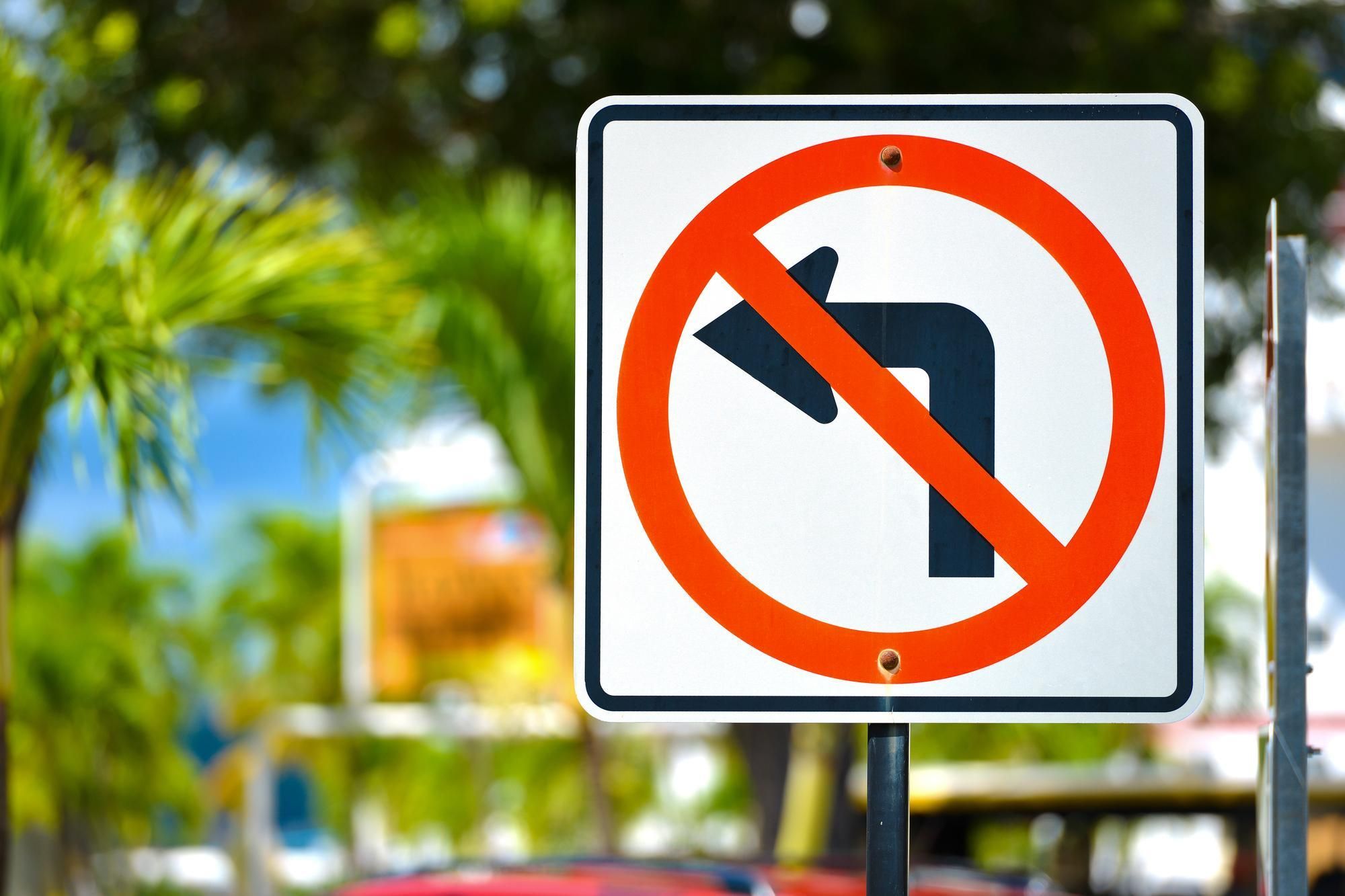 Traffic signage prohibiting left turns at a busy intersection; palm trees in the background.